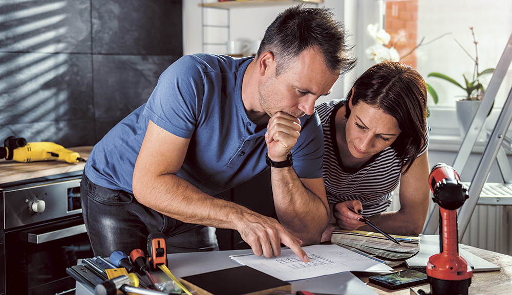 A couple examine house plans in their kitchen.