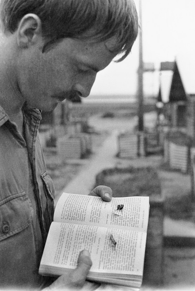 Young man in battle fatigues looking at book that has bullet hole through it.