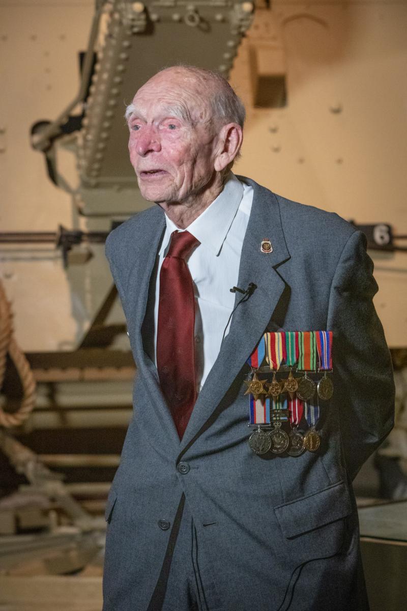 Elderly veteran standing in front of Second World War display.