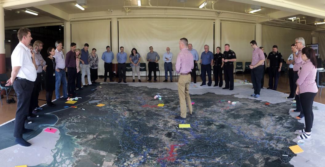 Man standing on very large map talking to about 20 people