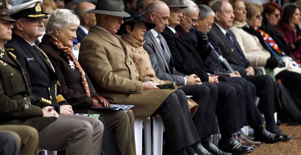 A row of people in suits and uniforms seated with heads bowed.