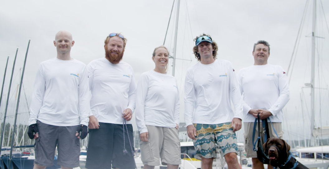Four men, a woman and a dog posing with yachts in background.