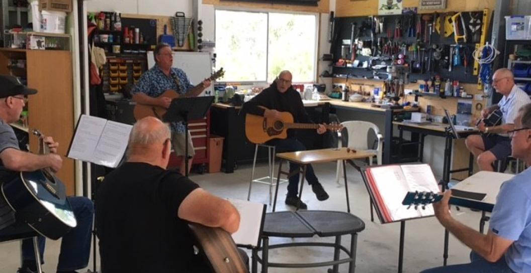 Group of middle-aged men playing guitars in a circle indoors