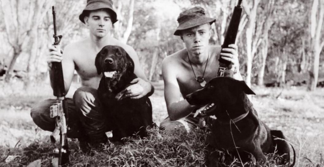 Two young men holding assault rifles with black labradors