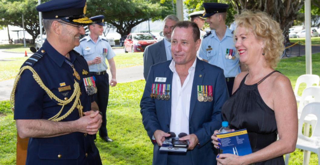 A man in Air Marshal's dress uniform chats with a man and woman in a marquee.