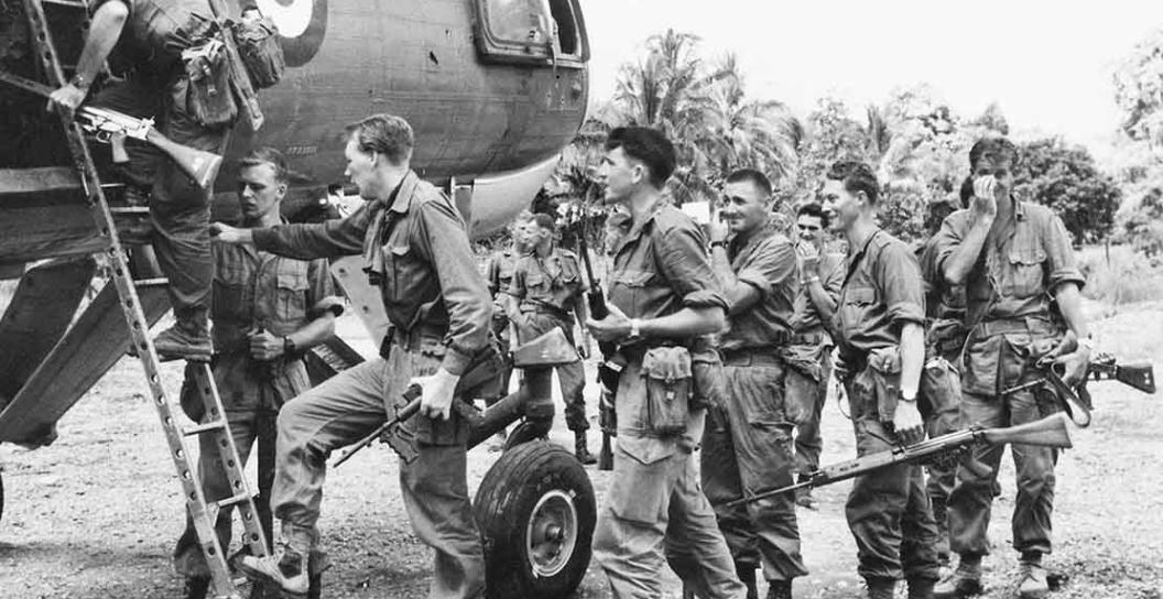 Half a dozen or so soldiers board a helicopter in the jungle