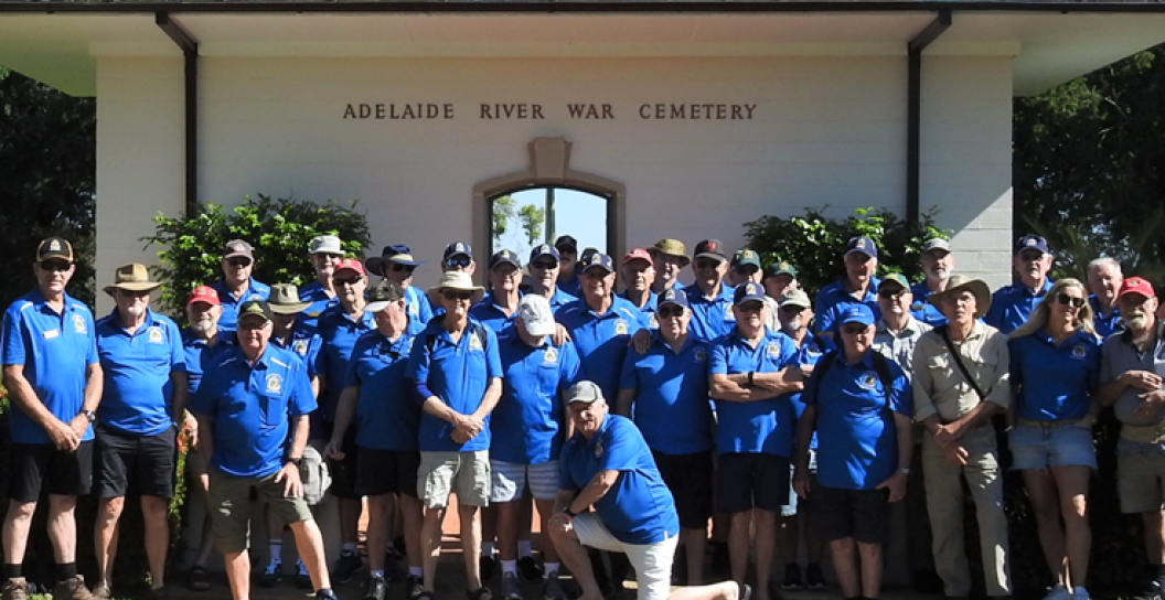 Forty or fifty men in blue T-shirts in group photo at entrance to Adelaide Creek War Cemetery