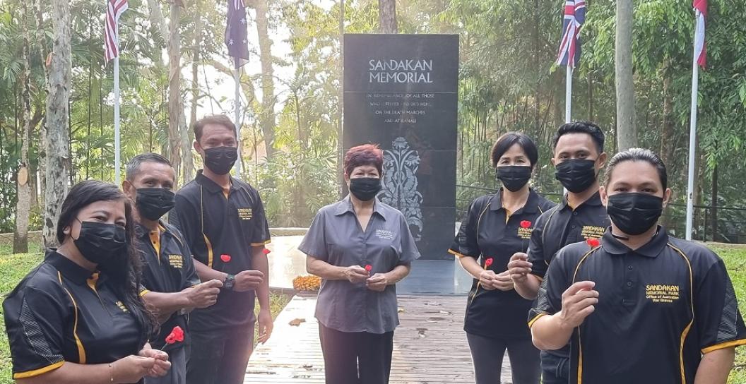 Seven Asian people posing in front of black obelisk surrounded by jungle.