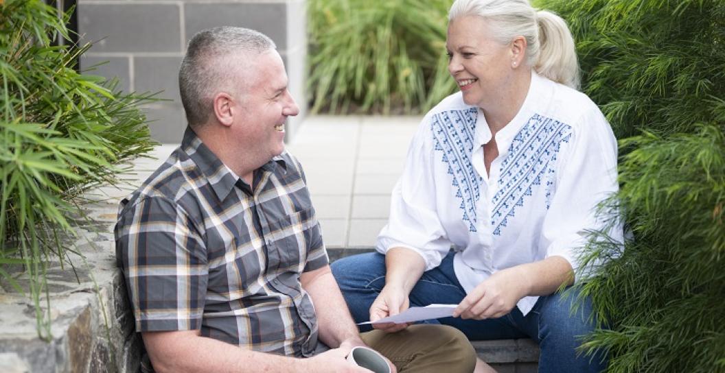 An ageing couple chat on steps in a back garden