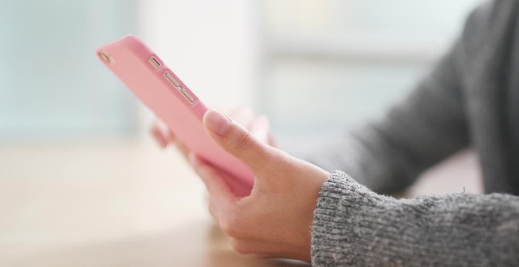 Close up of a woman's hands holding a mobile phone in a pale pink case