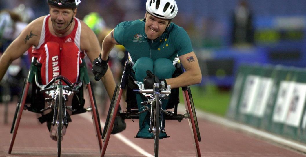 Two men in racing wheelchairs, grimacing with effort