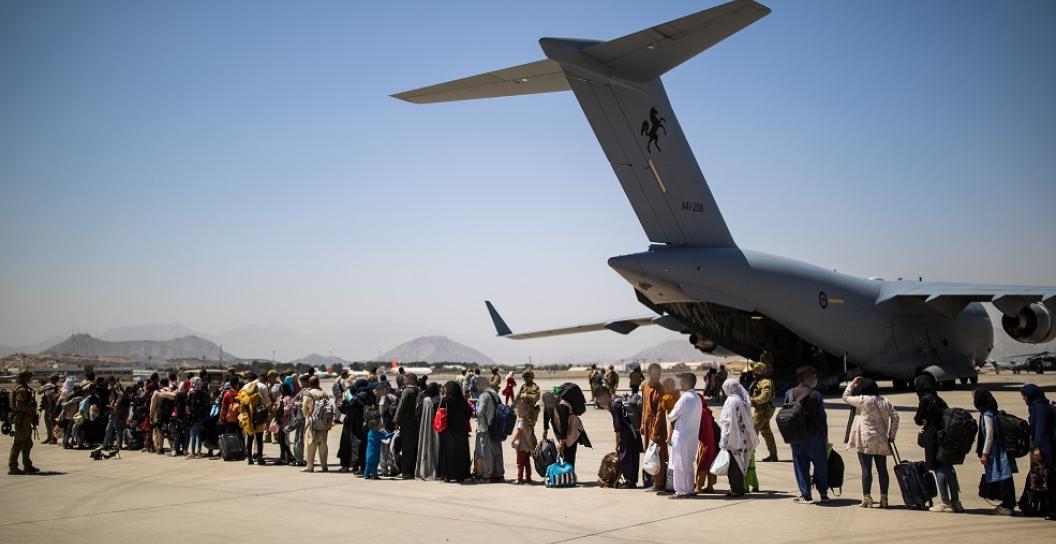line of refugees on tarmac next to large transport plane