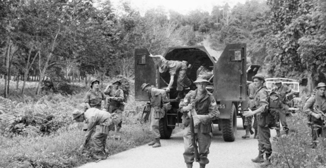 Soldier faces camera while around 10 others move around armoured truck