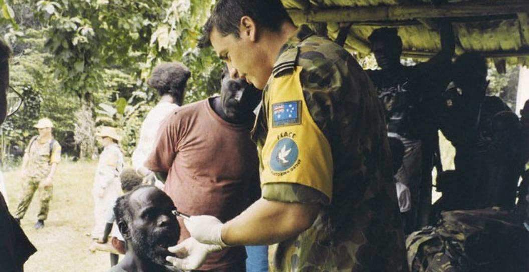 Soldier providing medical care to local man, perhaps in PNG