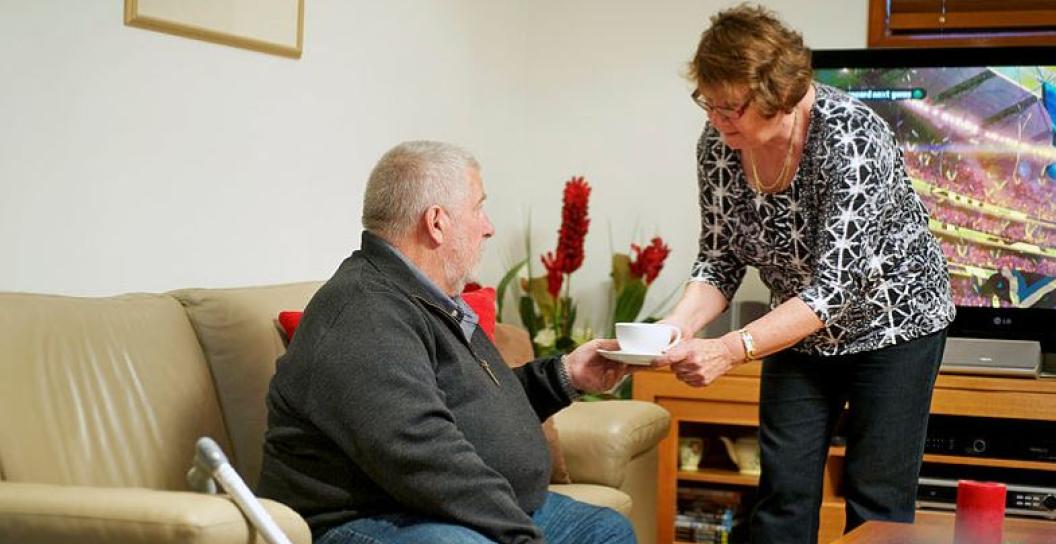 Woman serves tea to ageing man on sofa