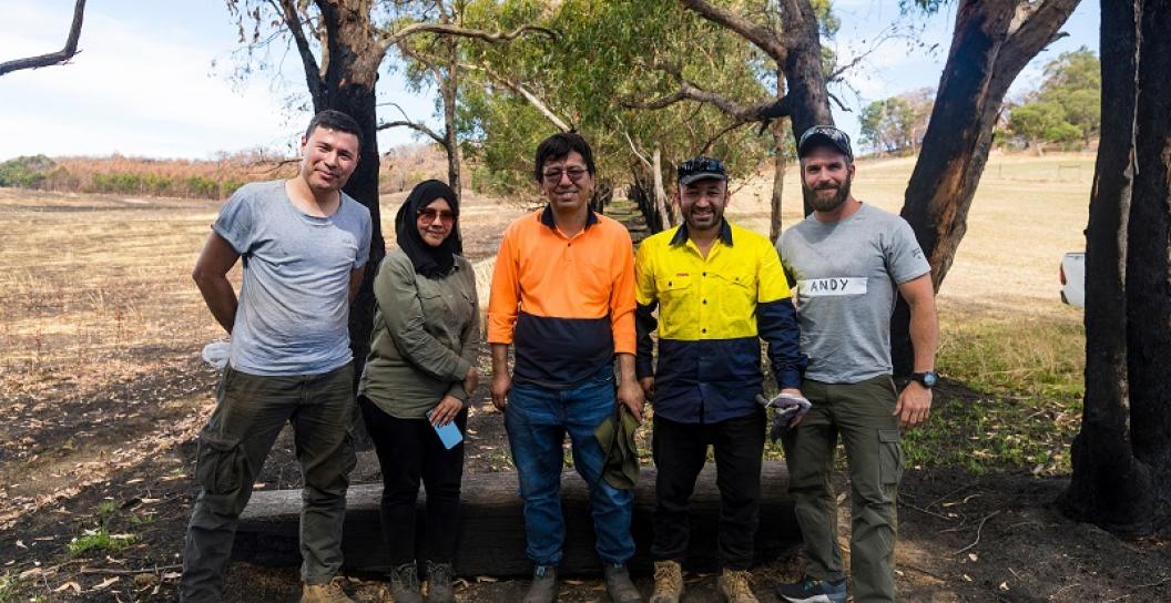 Five people smiling with trees in background. Four men and a woman with head scarf