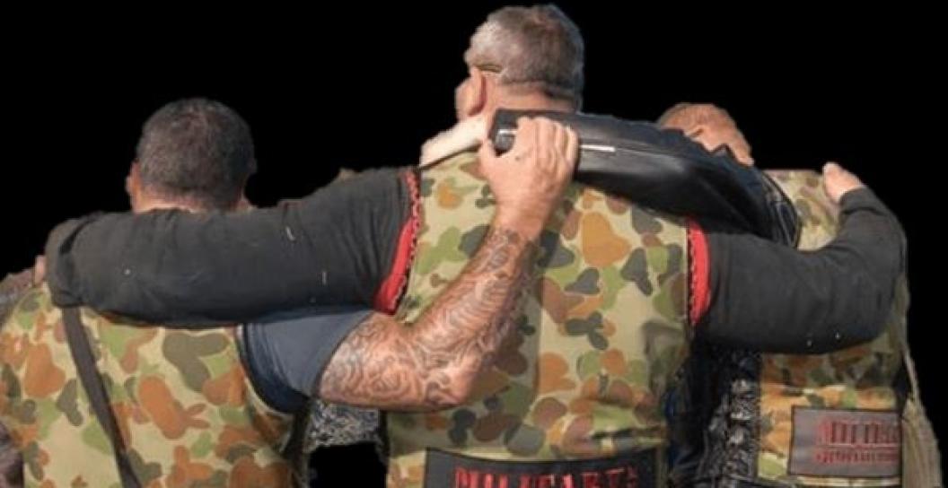 Photo from behind of three men in biker and Army gear with arms round each other's shoulders