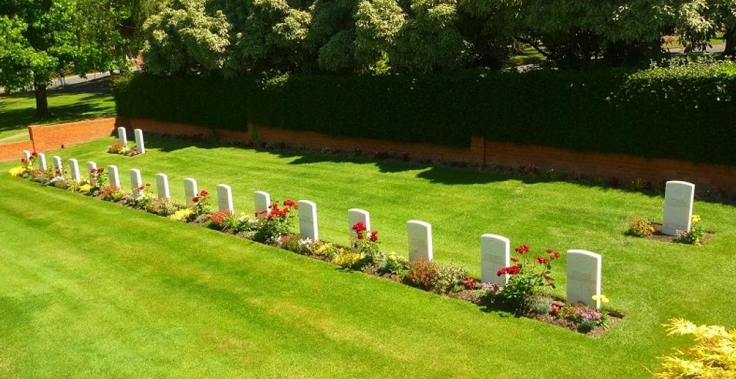 Manicured lawn with 19 white headstones and trees behind them
