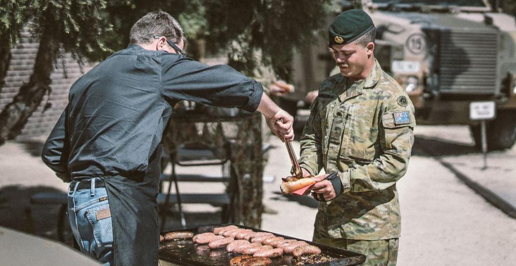 Civilian at barbecue handing soldier a sausage