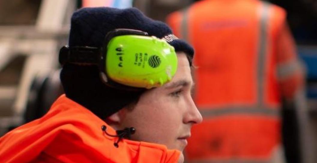 Profile shot of young worker wearing fluoro jacket and ear protection