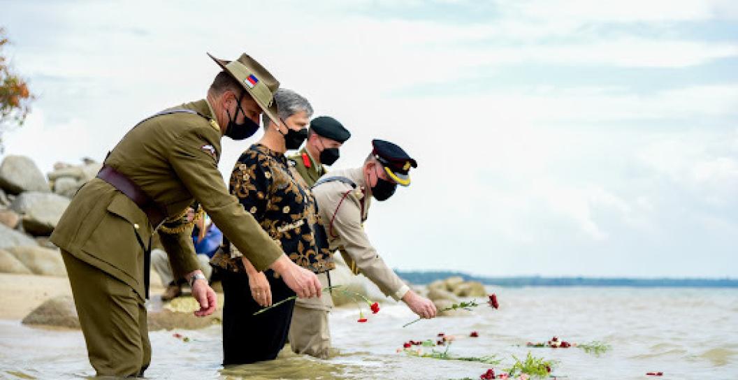 A civilian woman and three men in uniform knee-deep in the sea lay wreaths