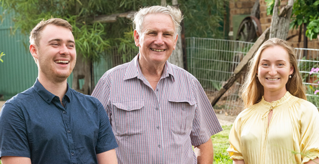 An older man with a young man on his right, and young woman on his left, all smiling, in a garden