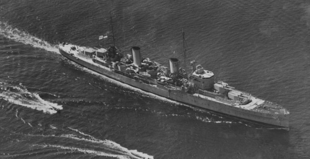 Aerial photo of Second World War cruiser on calm water surrounded by smaller boats