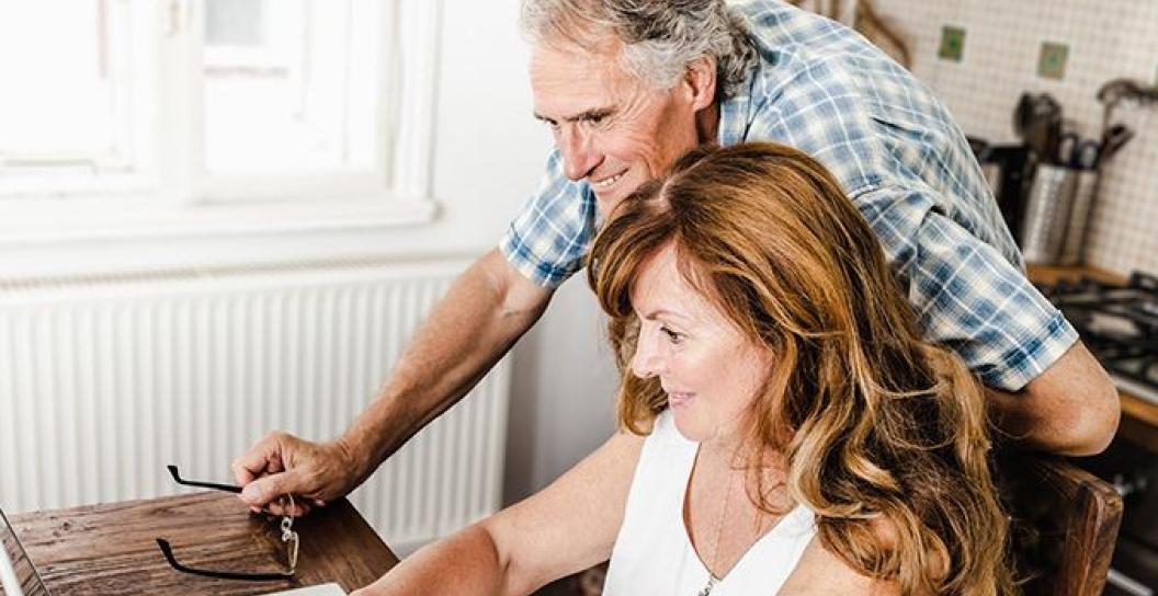 Older man looks over the shoulder of middle aged woman at a computer