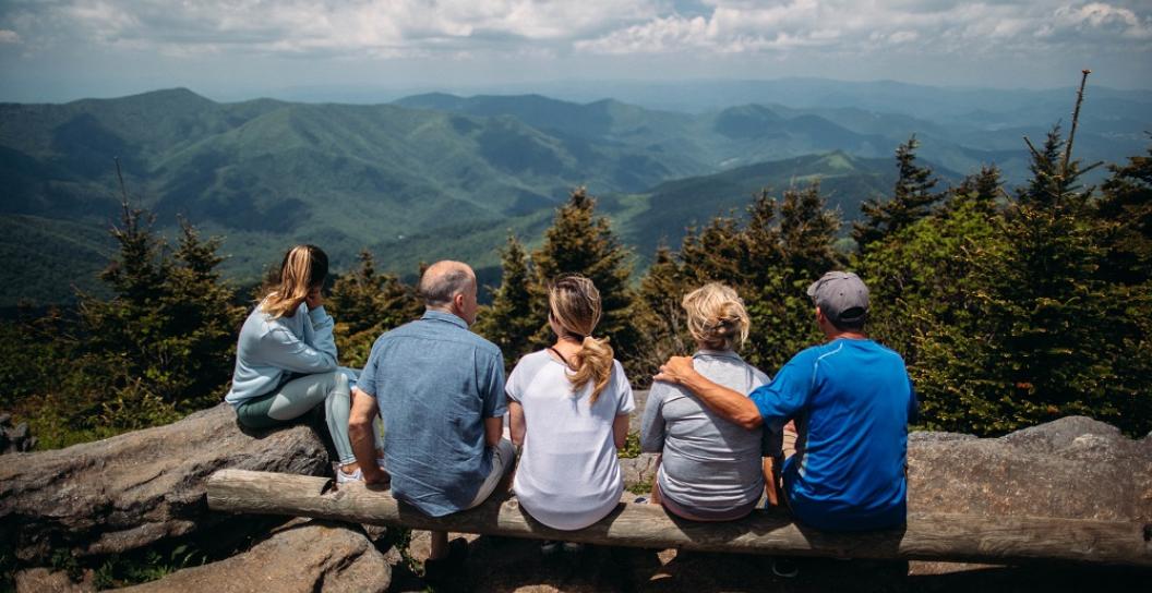 Family of five sitting on cliff top looking over view of wooded hills