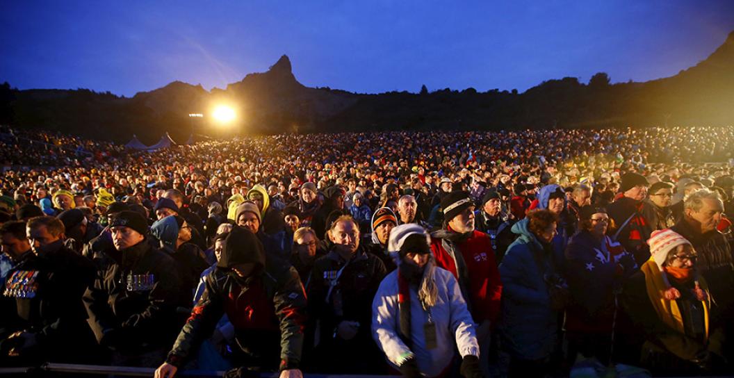 Vast seated crowd in foreground with rough terrain in background, at dawn