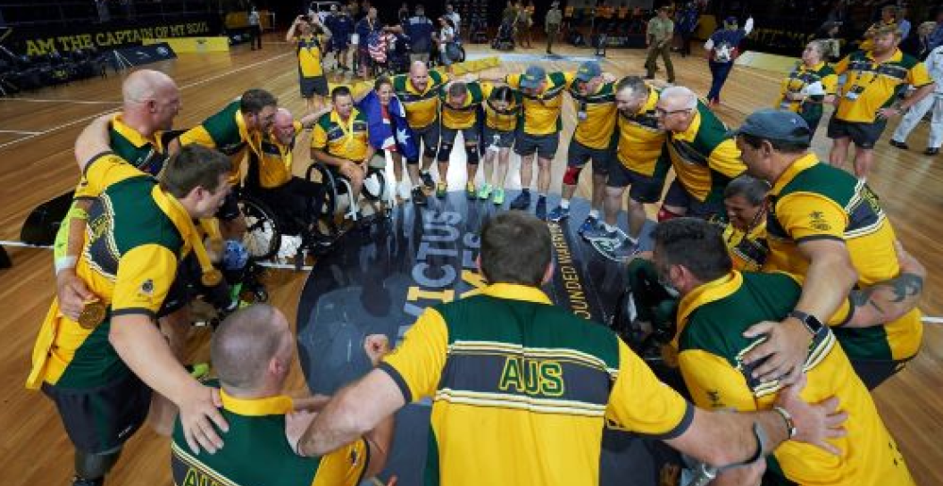 A ring of basketballers gather together in a huddle on a basketball court or similar