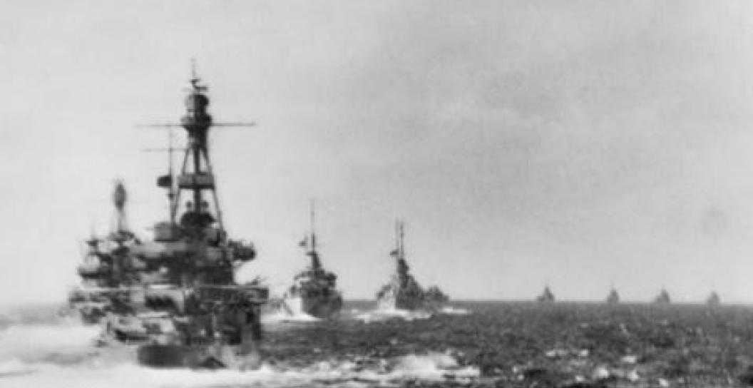 Grainy black and white photo of five warships sailing in a column