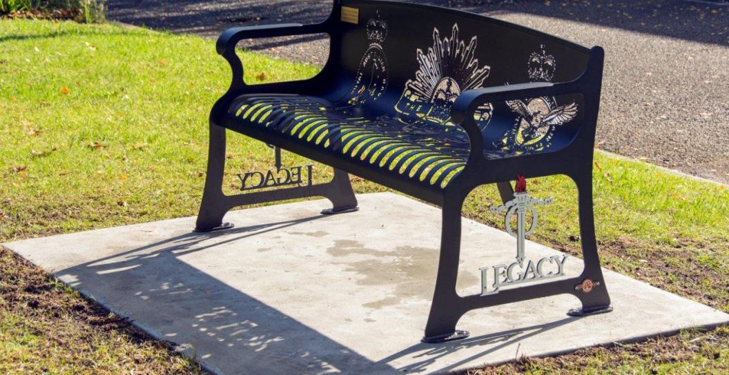 Carved metal bench on concrete platform surrounded by grass
