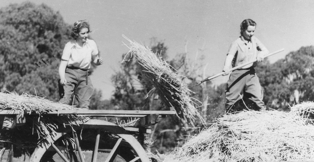 Two young women moving hay around on a cart