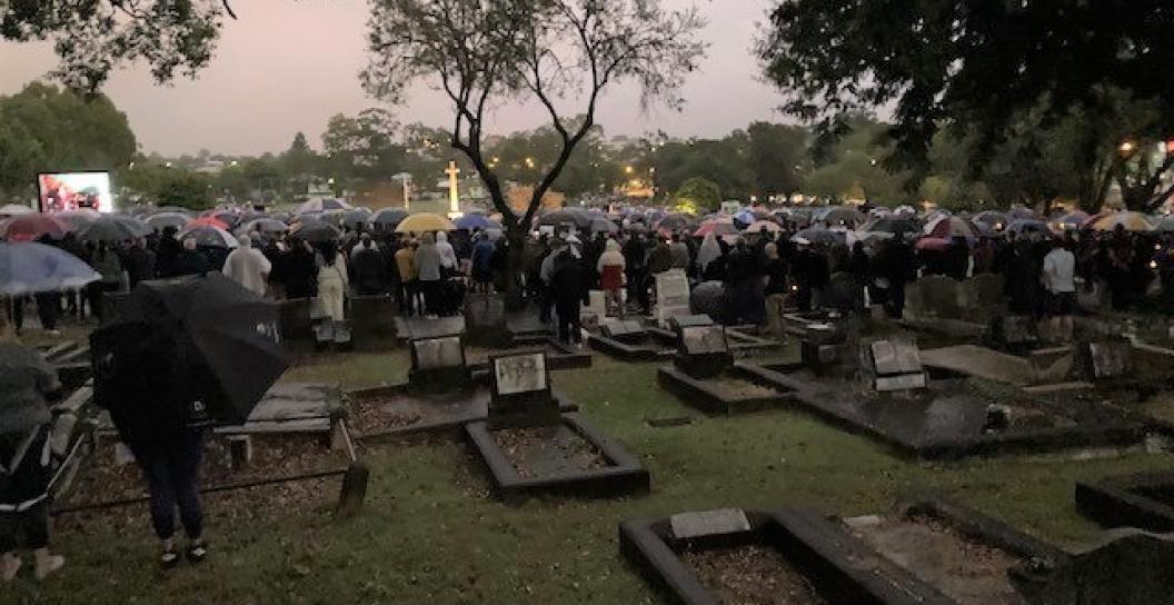 Dim photo of people with umbrellas gathered in cemetery