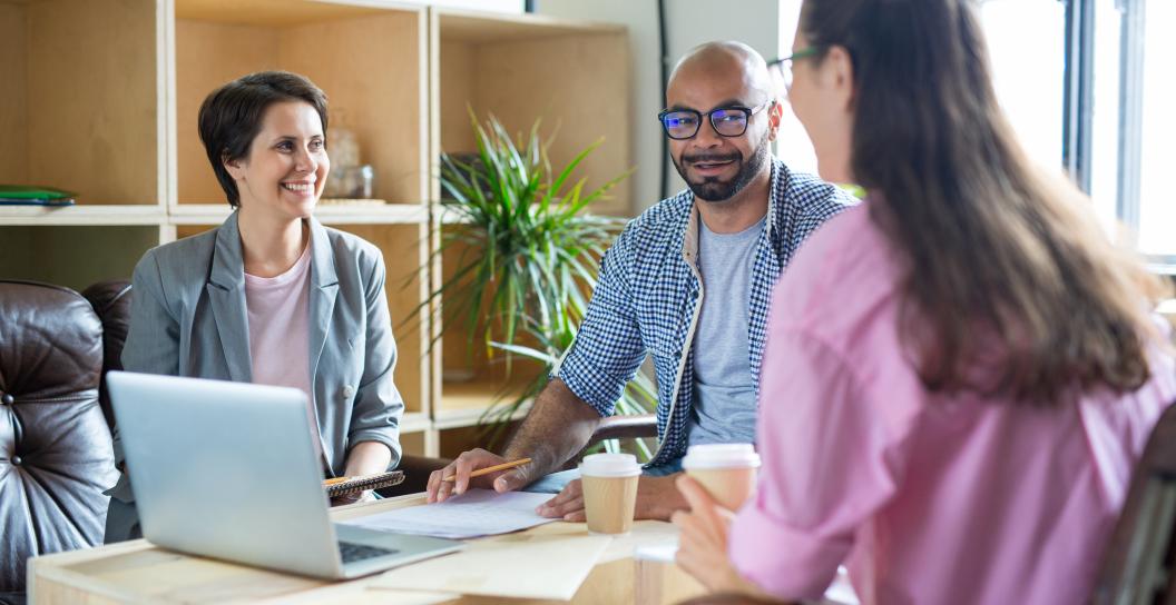 Three people are sitting around an open laptop, all are smiling