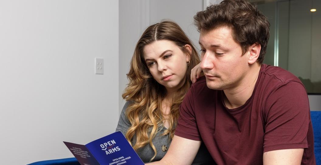 Young couple on sofa look at Open Arms brochure