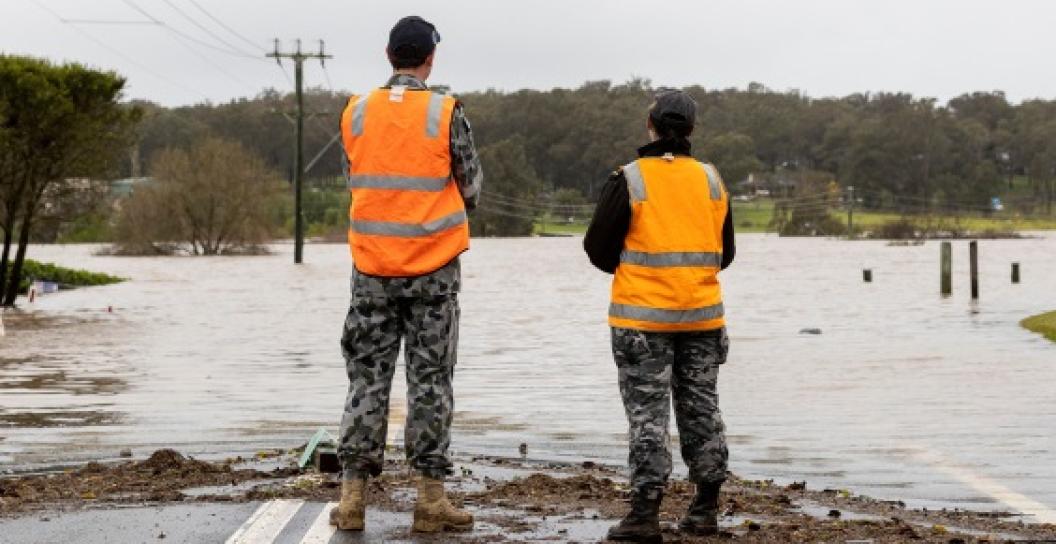Two ADF personnel in high-vis vests survey flooded road