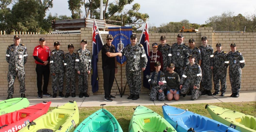 Men and children, mostly in naval uniform, pose in front of kayaks