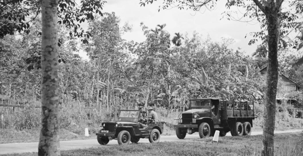 A GS quarter ton truck (Jeep) being followed by a GMC, CCKW-353 two and a half ton truck, both laden with unidentified troops from 2nd Battalion, The Royal Australian Regiment (2RAR), travelling down a road in Malaya