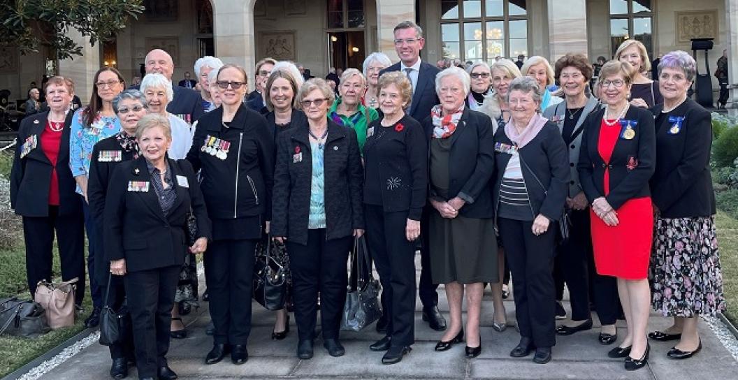 One man and about twenty older women pose for photo outside gothic sandstone house