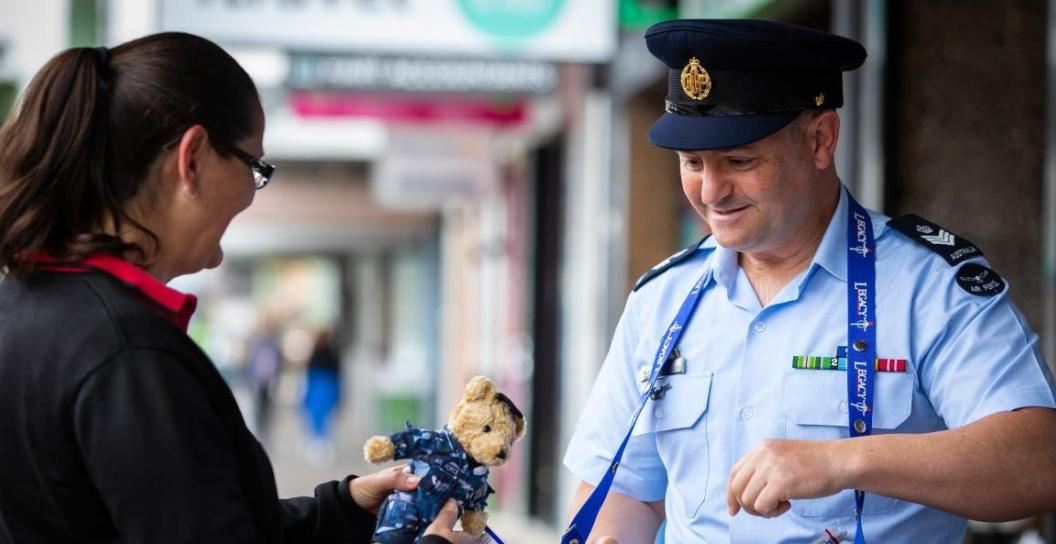 Man in RAAF uniform sells a Legacy bear to a woman