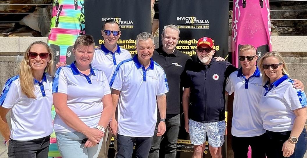Nine men and women pose on beach in front of Invictus signage