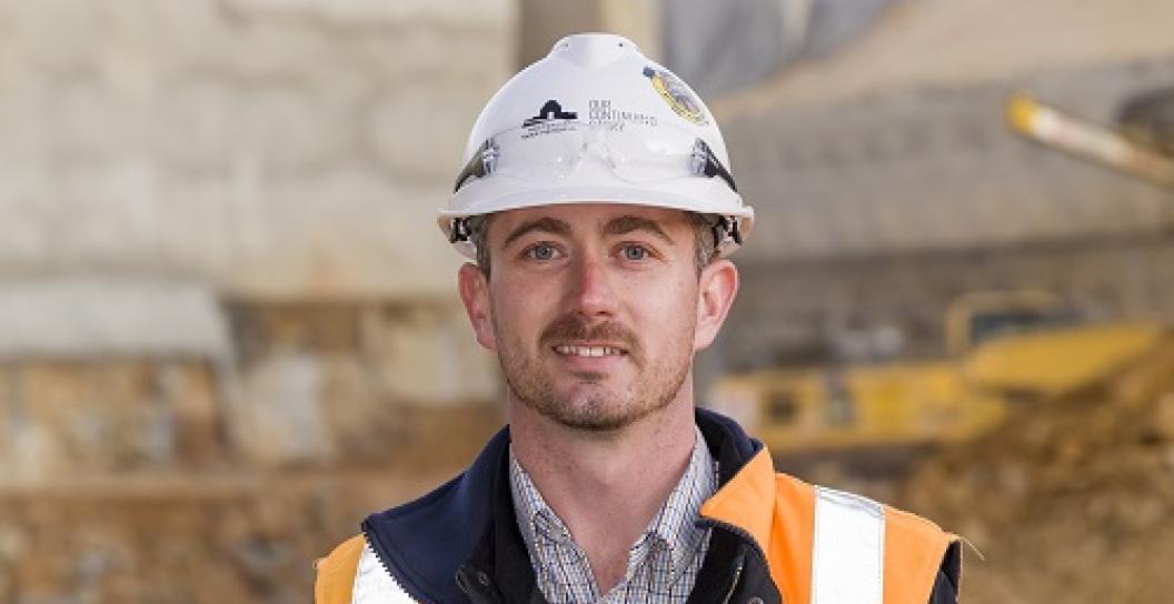 You man in hard hat and high vis vest posing for camera on a construction site.
