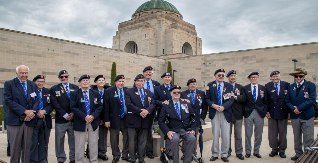 About 15 older men posing in front of Australian War Memorial