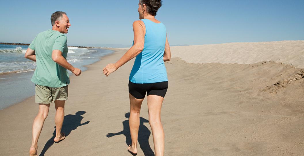 Two people are jogging along the beach, facing away from the camera