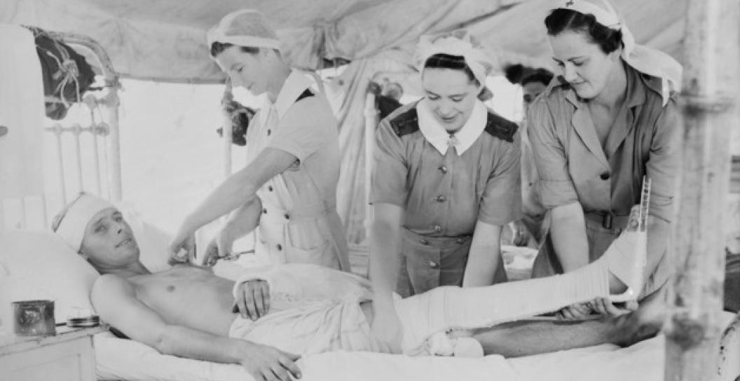 Three women in nursing uniforms attending to a wounded man on a hospital bed