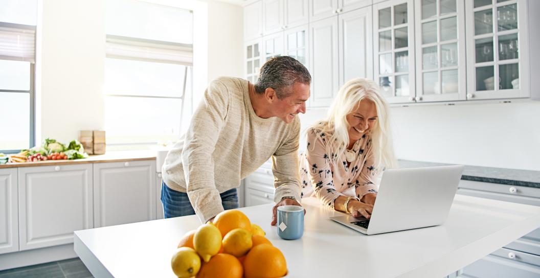 Two adults review information on a computer at the kitchen bench