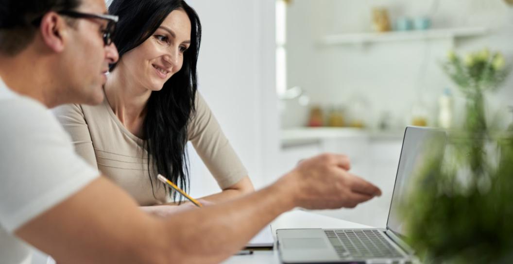 Two adults review information on a computer at the kitchen bench