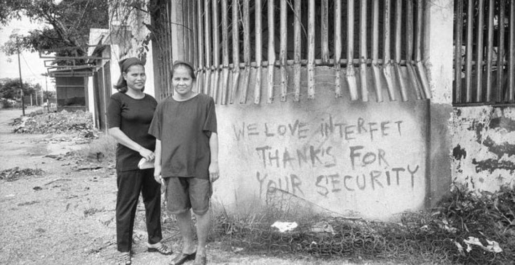 Two East Timorese women stand next to wall that the words 'We love interfet thanks for your security' written on it